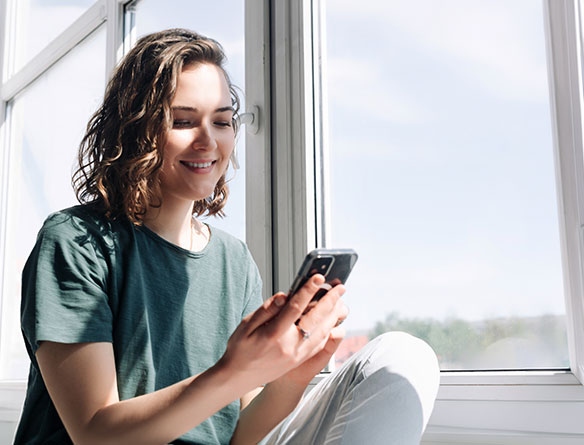 Eine Studentin sitzt am Fenster und informiert sich mit dem Smartphone &uuml;ber Studien- oder Karrierem&ouml;glichkeiten.