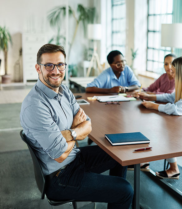 Ein Mann sitzt selbstbewusst vor einer Gruppe im B&uuml;ro und vermittelt einen professionellen Einstieg in Arbeitswelt, Team und Karriere.
