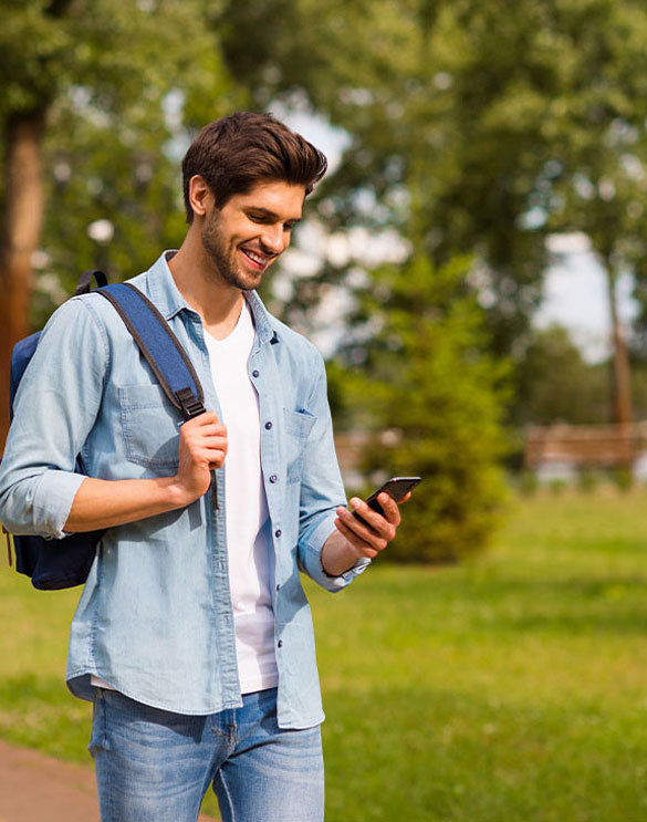 Ein Student mit Rucksack nutzt sein Smartphone im Freien und informiert sich unterwegs &uuml;ber Studieninhalte.
