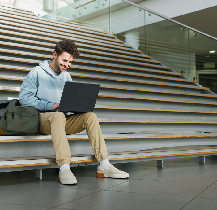 Ein Student sitzt mit einem Laptop auf einer Treppe und arbeitet an Studieninhalten.